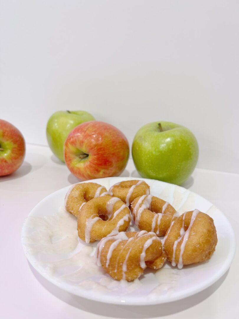 A plate of donuts with glaze placed beside apples